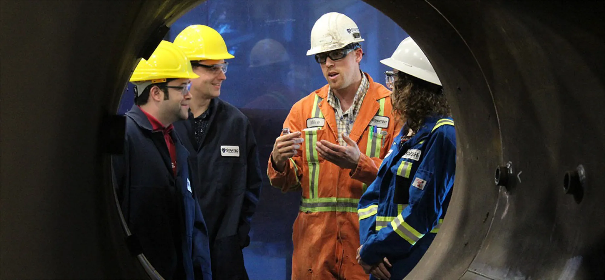 A Picture of a group of worker having a discussion, we are looking at them through a big pipe.