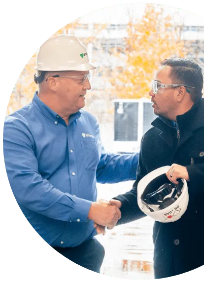 A picture of people walking together in a line in an industrial plant. There are two men shaking hands as they walk